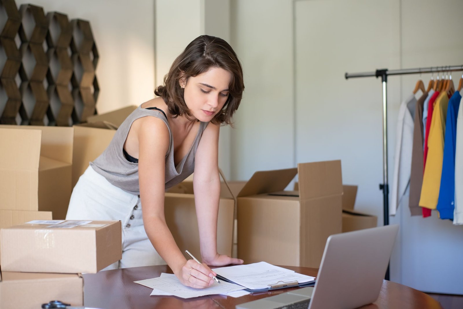 Empreendedora organizando a loja de roupas online em casa, entre caixas e o notebook