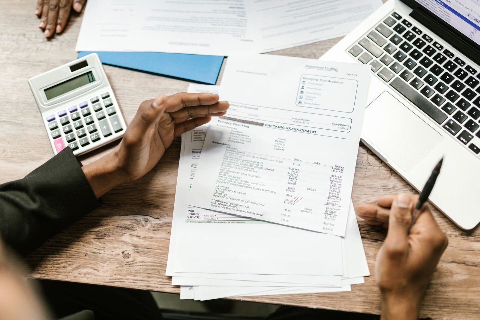 Mãos segurando relatórios financeiros ao lado da calculadora e do notebook