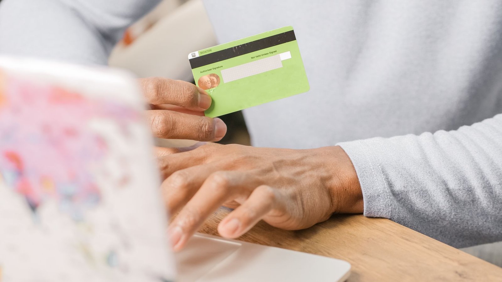 Cliente segurando o cartão para concluir uma compra no notebook