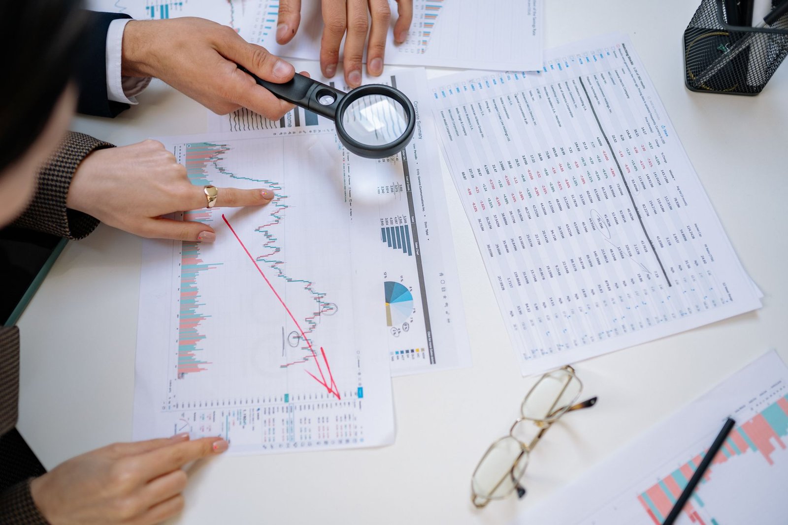 Mãos apontando para relatórios financeiros sobre a mesa de reunião
