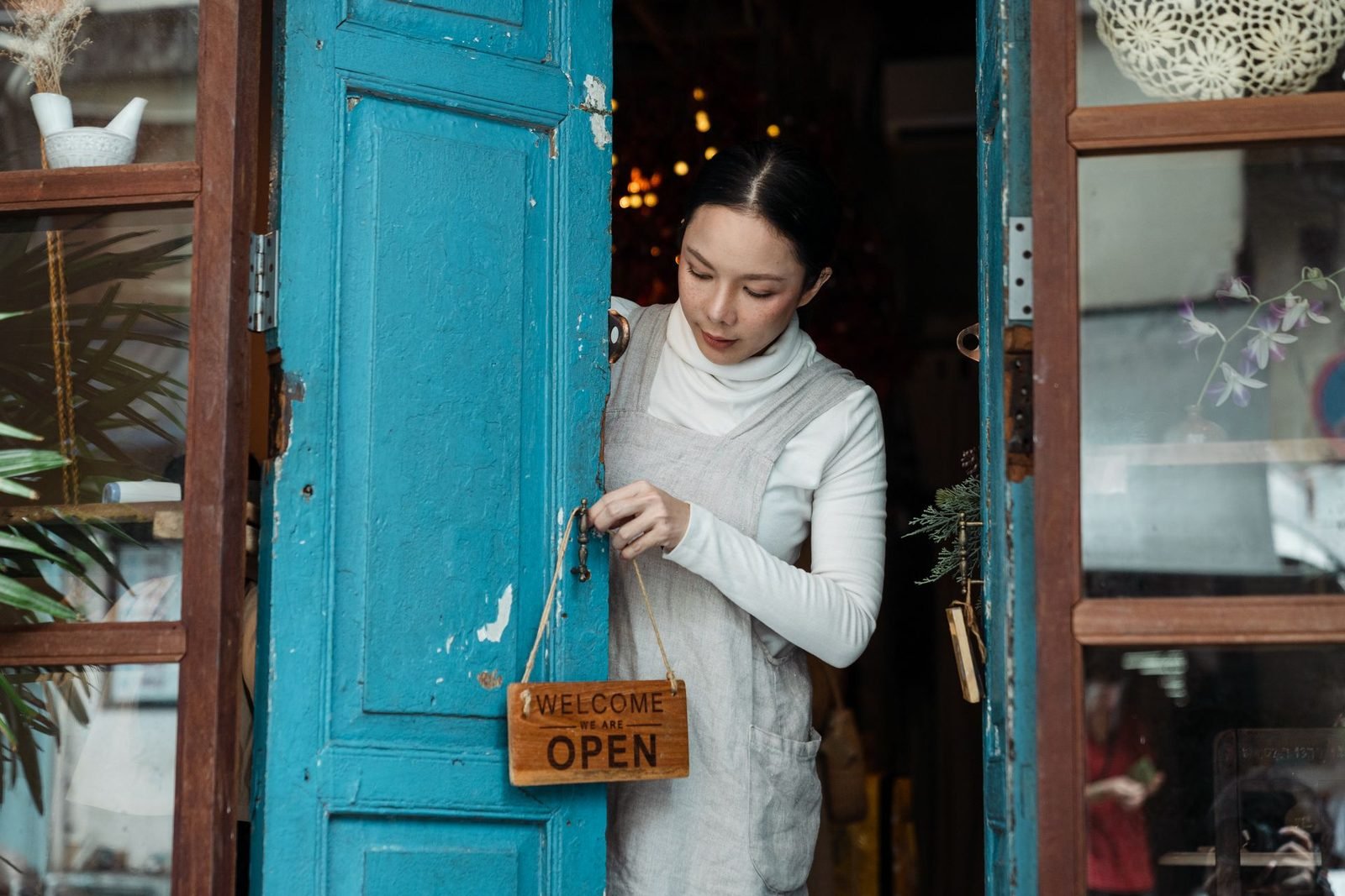 Empreendedora ajustando a placa de aberto na porta azul do seu café