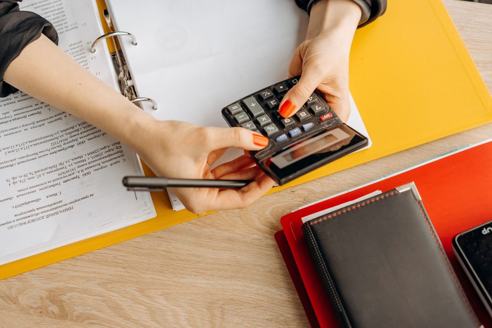 Mãos usando calculadora sobre uma mesa cheia de documentos e pastas