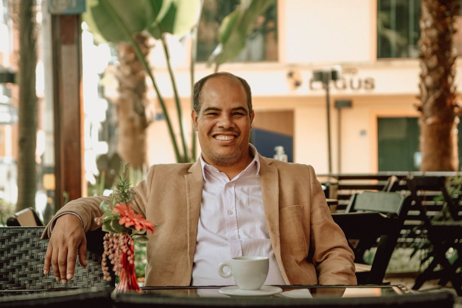 Homem de terno sorrindo em uma mesa de café ao ar livre
