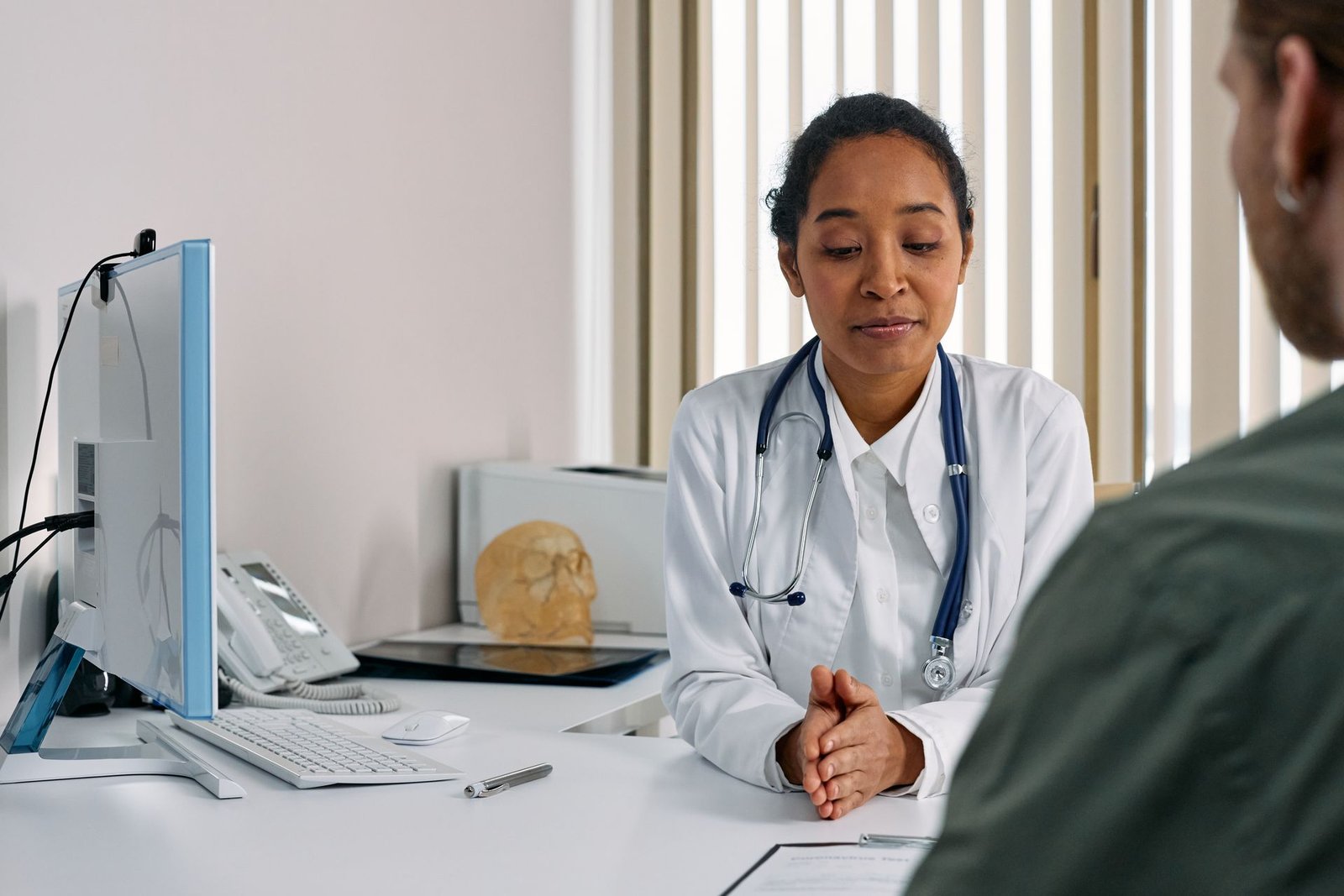 Médica de jaleco branco atendendo um paciente no consultório