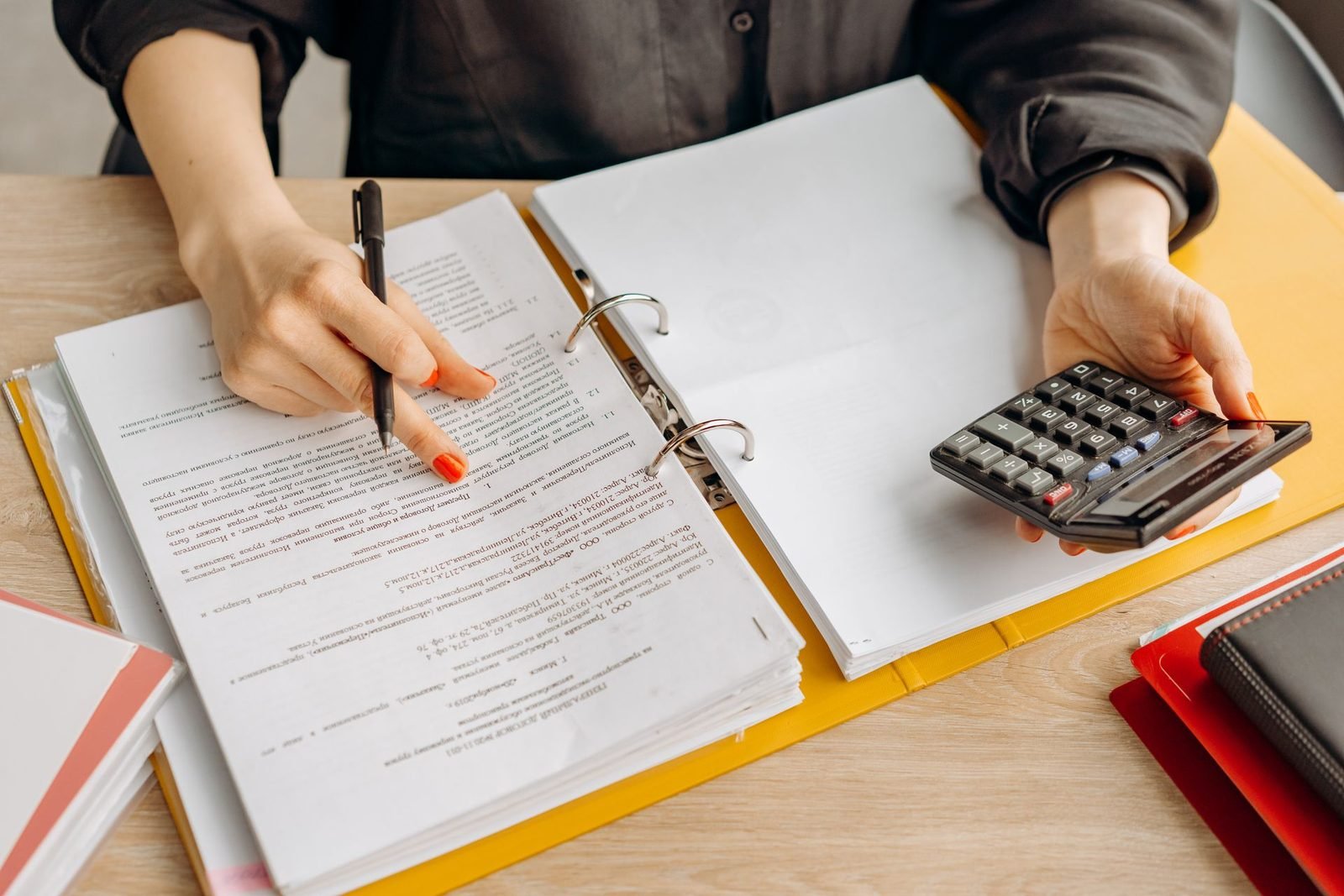 Empresária revisando relatórios e usando a calculadora sobre a mesa de madeira
