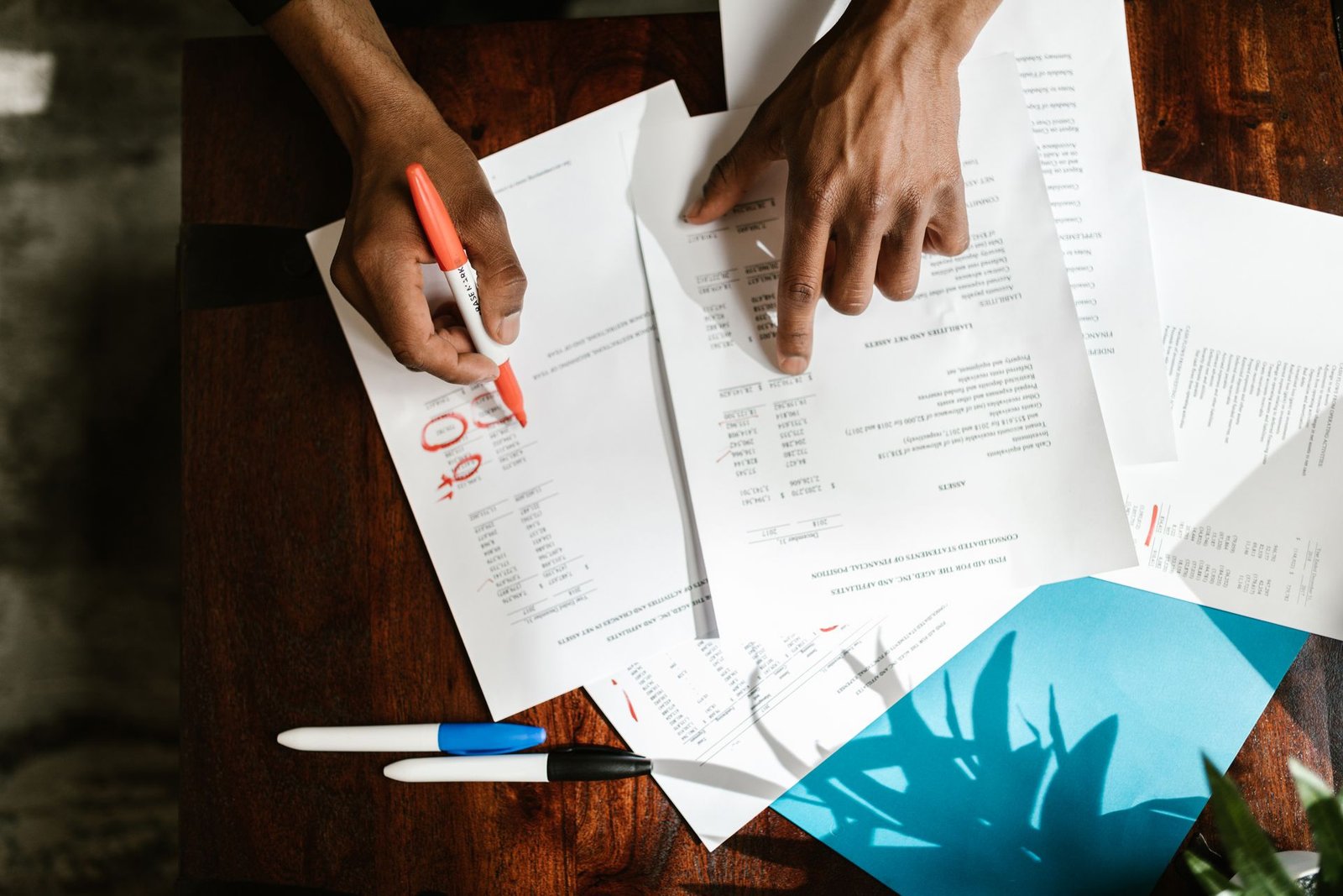 Vista de cima de mãos marcando valores em relatórios financeiros sobre a mesa