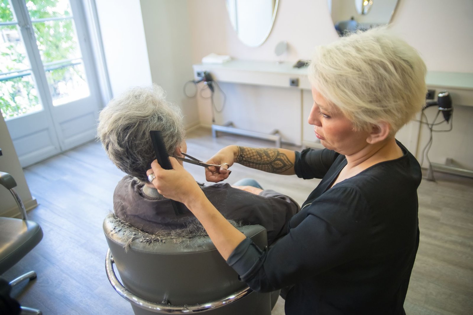 Cabeleireira cortando o cabelo de uma cliente idosa em um salão claro