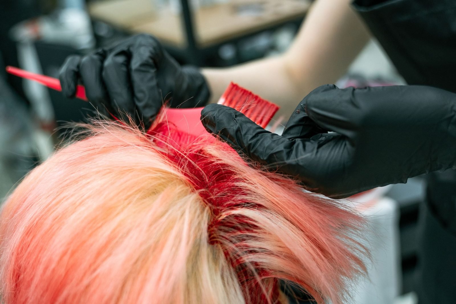 Mãos com luvas pretas aplicando coloração em mechas de cabelo
